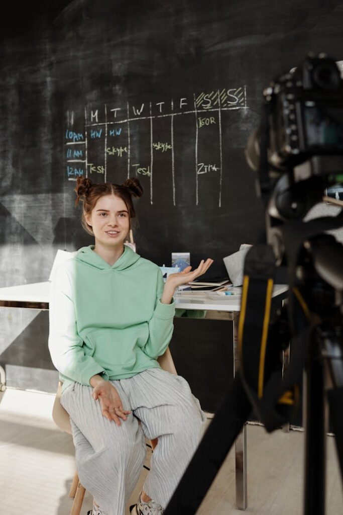 Teenage girl recording a vlog indoors with a camera setup and chalkboard background.